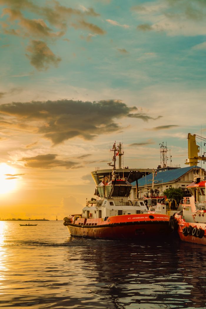 The Art of Drawing Readers In: Your attractive post title goes here Colorful sunset at Makassar Harbor, South Sulawesi, with tugboats and a dramatic sky.